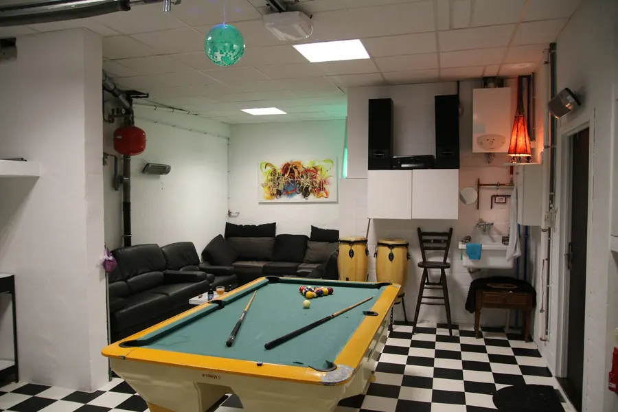 De spelkamer: biljarttafel, darts, leren zetels en een geblokte vloer